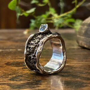 Photograph of a large oxidized and textured ring with a set light blue topaz.