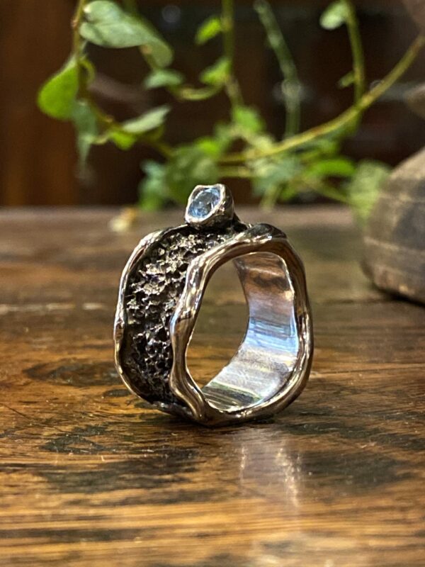 Photograph of a large oxidized and textured ring with a set light blue topaz.